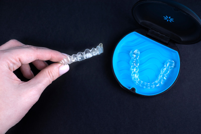 Woman holding invisible transparent aligners invisalign or plastic orthodontic braces. Black package with a box, clear-plastic retainers